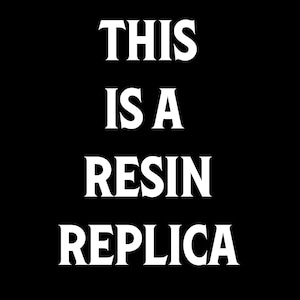 May include: Black background with the white text "THIS IS A RESIN REPLICA" in a bold, serif font. The text is centered and takes up most of the image.