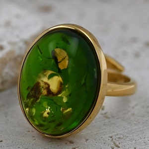 May include: A gold ring featuring a large oval green stone set in the centre. The stone contains a golden insect trapped inside.