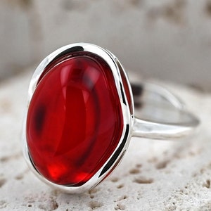 Peut inclure: Une bague en argent avec une grande pierre rouge de forme ovale sertie dans une bélière en argent.