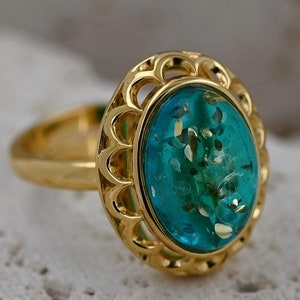May include: A gold ring featuring a large oval turquoise blue stone set within a decorative gold filigree frame.