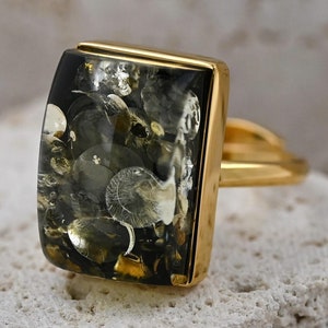 May include: A gold ring with a rectangular green and black stone. The stone has a unique pattern of inclusions.