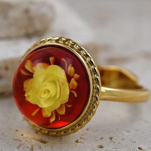 Può includere: Un anello d'oro con una rosa rossa e gialla incastonata in ambra.