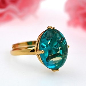 May include: A gold ring featuring a large oval teal blue gemstone. The gemstone has a swirling pattern within it.