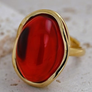 May include: A gold ring with a large, oval-shaped, red gemstone.