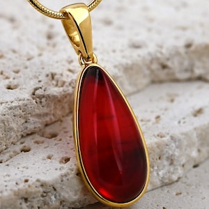 Op de afbeelding: Een gouden ketting met een traanvormige hanger met een dieprode edelsteen.