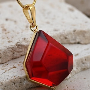 Può includere: Una collana con catena d'oro con un ciondolo di pietra rossa. Il ciondolo è sfaccettato e ha una forma geometrica.