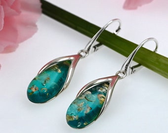 May include: A pair of silver dangle earrings with teardrop-shaped turquoise blue glass beads with gold flecks. The earrings are hanging on a green stem.