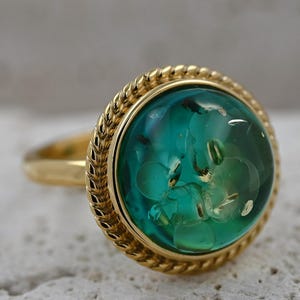 May include: A gold ring featuring a large, round, green gemstone. The gemstone has a rope-like border and is set in a gold band.