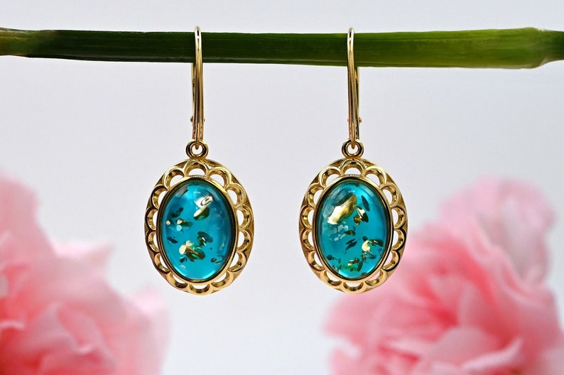 May include: Gold earrings with a turquoise oval-shaped stone set in a gold filigree frame. The stone has gold flecks throughout.