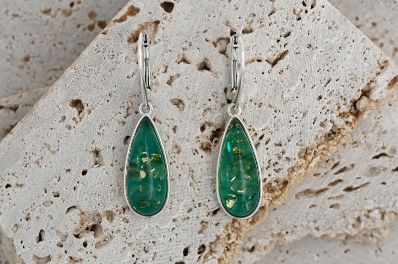 May include: A pair of silver dangle earrings with green teardrop-shaped resin stones. The stones have a sparkly gold fleck throughout.