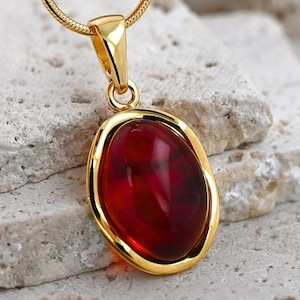 May include: A gold pendant necklace featuring a red oval-shaped gemstone set in a gold bezel.