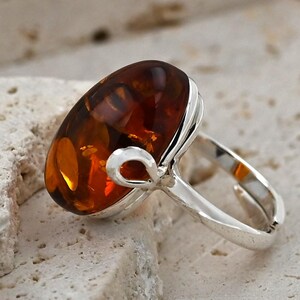 May include: A silver ring with a large, oval amber gemstone. The amber is a warm, translucent brown and orange colour. The ring has a simple, polished silver band and a decorative loop detail.