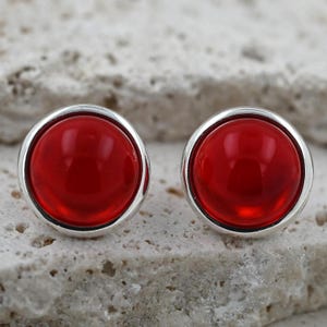 Könnte beinhalten: Ein Paar silberne Ohrstecker mit roten runden Cabochonsteinen.