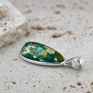 May include: A teardrop-shaped pendant with a silver setting. The pendant features a vibrant mix of green and gold hues, creating a unique and eye-catching design. This jewelry piece is suitable for everyday wear or special occasions.