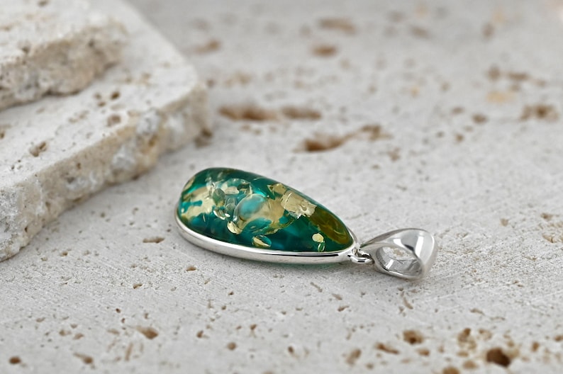 May include: A teardrop-shaped pendant with a silver setting. The pendant features a vibrant mix of green and gold hues, creating a unique and eye-catching design. This jewelry piece is suitable for everyday wear or special occasions.