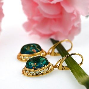 May include: Gold dangle earrings with a green oval-shaped stone set in a gold filigree frame. The stone has a blue and green color with gold flecks.