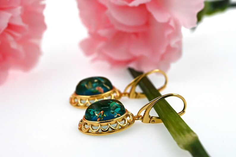 May include: Gold dangle earrings with a green oval-shaped stone set in a gold filigree frame. The stone has a blue and green color with gold flecks.