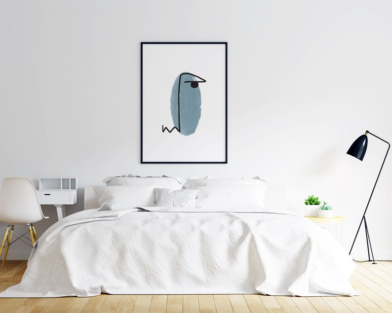 以下が含まれることがあります： 白い背景に青い楕円形と黒い線が描かれた、ミニマルな抽象的なデザインの黒枠のプリント。プリントは白い壁に掛けられており、白いベッドの上には白い寝具が敷かれています。