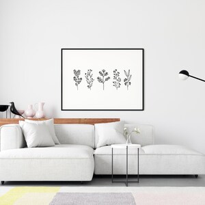 May include: A black and white line art print of five different floral sprigs in a black frame hanging on a white wall above a white sectional sofa with a white side table and a black floor lamp.