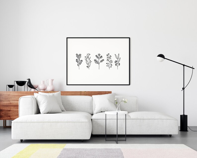 May include: A black and white line art print of five different floral sprigs in a black frame hanging on a white wall above a white sectional sofa with a white side table and a black floor lamp.