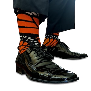Op de afbeelding: Een paar zwarte leren nette schoenen met oranje en zwarte sokken met vlindermotief. De sokken hebben een zwarte achtergrond met oranje vlindervleugels.