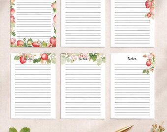 May include: A collection of six lined note pads with strawberry and floral designs. The pads have the words "Notes" and "Note" printed on them. A bowl of strawberries, a cup of tea, and a gold pen are also in the image.