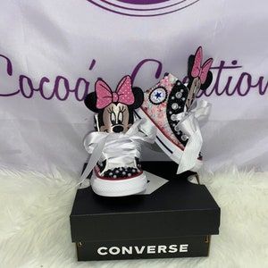 May include: A pair of white Converse trainers with a pink and black Minnie Mouse design. The trainers are decorated with rhinestones and have white satin laces. The trainers are in a box with the Converse logo.