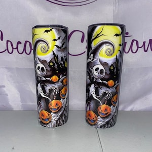 May include: Two black and white stainless steel tumblers with a Halloween themed design featuring Jack Skellington from The Nightmare Before Christmas. The design includes a yellow moon, a spooky tree, and pumpkins.