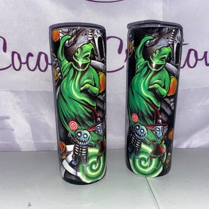 May include: Two black and green stainless steel tumblers with a Halloween theme. The tumblers feature a green ghost with a black hat and a swirl design. The ghost is surrounded by smaller characters with black hats and green faces.