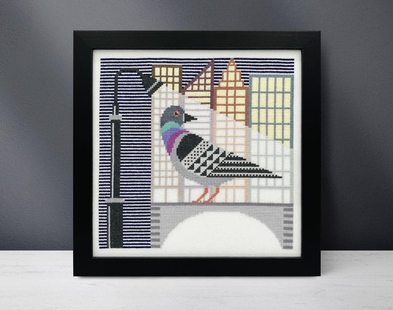 Puede incluir: Un patr&oacute;n de punto de cruz de una paloma posada en un puente frente a un horizonte urbano. La paloma es gris con marcas moradas y blancas. El horizonte urbano est&aacute; formado por edificios con ventanas de diferentes colores.