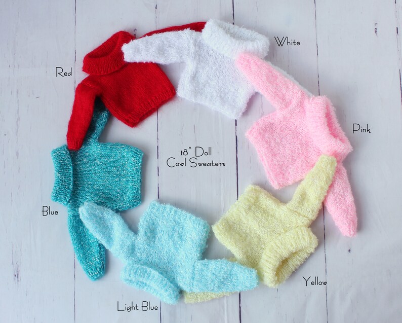 May include: Seven 18 inch doll cowl sweaters in various colors: red, white, pink, blue, light blue, yellow.  The sweaters are arranged in a circle on a white wooden background.  18" Doll Cowl Sweaters