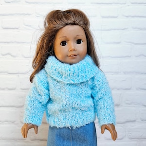 May include: A doll wearing a light blue fuzzy sweater with a turtleneck and a denim skirt.