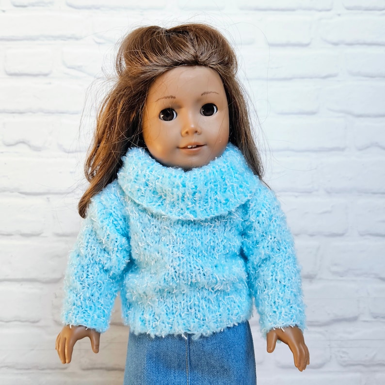 May include: A doll wearing a light blue fuzzy sweater with a turtleneck and a denim skirt.