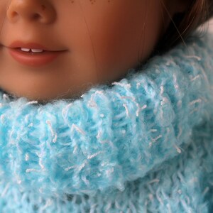 May include: A close-up of a doll wearing a light blue fuzzy turtleneck sweater.