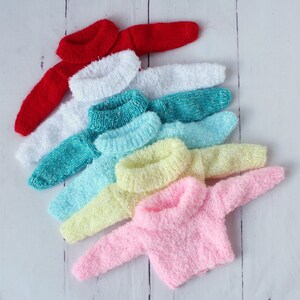May include: A stack of seven colorful knitted sweaters in various shades of red, white, teal, light blue, yellow, and pink. The sweaters are arranged in a rainbow pattern, with the red sweater on top and the pink sweater on the bottom.