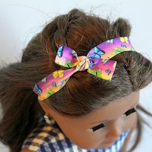 May include: A doll with brown hair wearing a headband with a rainbow and butterfly pattern.