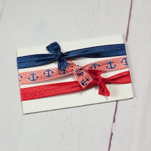 May include: Three hair ties with a nautical theme. One is navy blue, one is red with white polka dots and anchors, and one is red with white anchors.