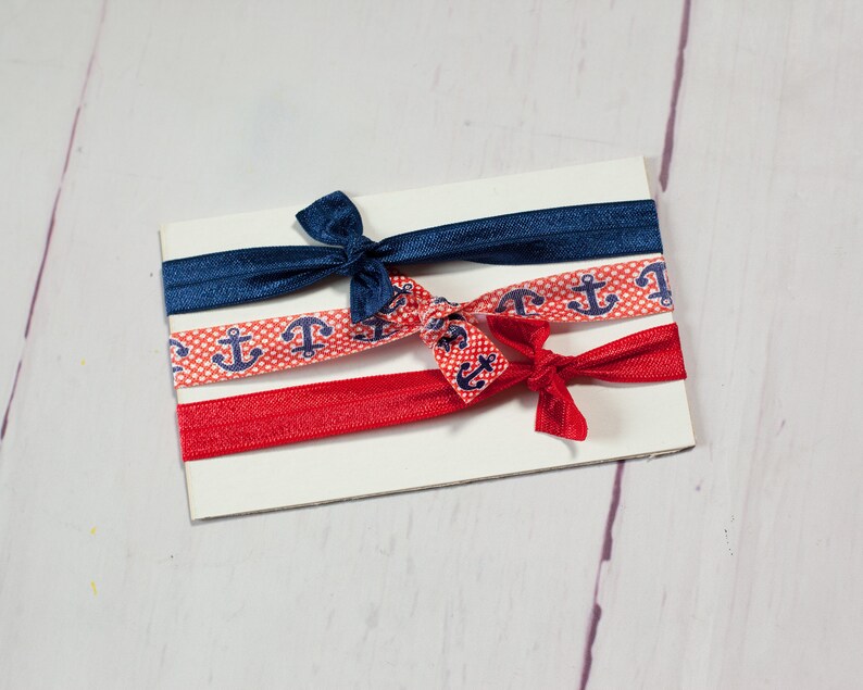 May include: Three hair ties with a nautical theme. One is navy blue, one is red with white polka dots and anchors, and one is red with white anchors.