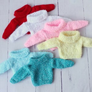 May include: Six colorful knitted sweaters with turtleneck collars. The sweaters are arranged in a stack, with the red sweater on top and the turquoise sweater on the bottom.