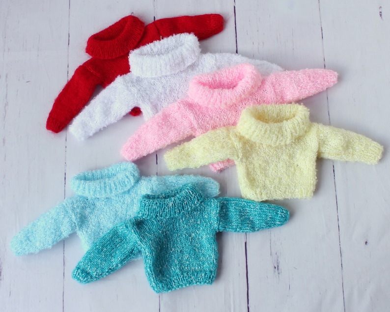 May include: Six colorful knitted sweaters with turtleneck collars. The sweaters are arranged in a stack, with the red sweater on top and the turquoise sweater on the bottom.