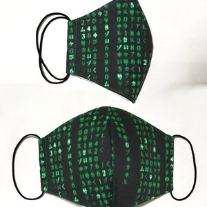 Puede incluir: M&aacute;scara facial negra con texto y n&uacute;meros verdes, que se asemejan a un c&oacute;digo inform&aacute;tico. La m&aacute;scara tiene lazos el&aacute;sticos para las orejas.