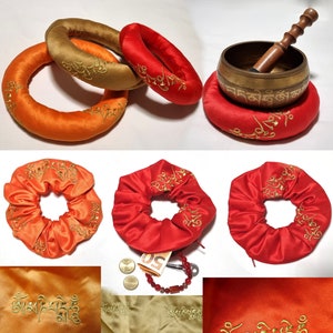 May include: A collection of meditation cushions and accessories. The image features three satin cushions in orange, gold, and red, with gold embroidery. A brass singing bowl and wooden mallet rest on a red cushion. Scrunchies and fabric samples are also shown.