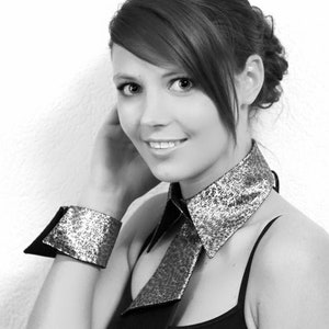 May include: A woman wearing a black top with a sparkly silver collar and matching bracelets. The collar is folded over and has a pointed shape.
