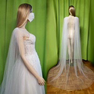 May include: A white tulle bridal cape with a long train. The cape is made of soft, sheer fabric and has a delicate, flowing design.
