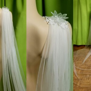 May include: A white tulle bridal cape with delicate floral lace appliques on the shoulders. The cape is 3 meters long and drapes elegantly.