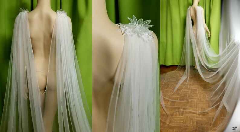 May include: A white tulle bridal cape with delicate floral lace appliques on the shoulders. The cape is 3 meters long and drapes elegantly.