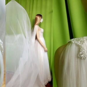 May include: A white tulle bridal veil with delicate lace trim. The veil is draped over a mannequin's shoulders and has a scalloped edge.