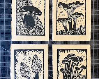 May include: Four black and white linocut prints of different types of mushrooms. The prints are on a brown paper background.
