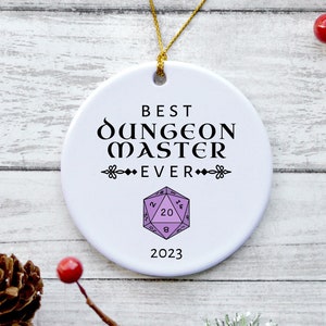 May include: White ceramic Christmas ornament with the text "Best Dungeon Master Ever" and a purple 20-sided die graphic. The year 2023 is printed below the graphic.