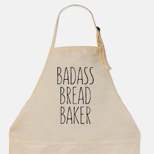 May include: A beige cotton apron with a large pocket and adjustable neck straps. The apron has black text that reads "BADASS BREAD BAKER".
